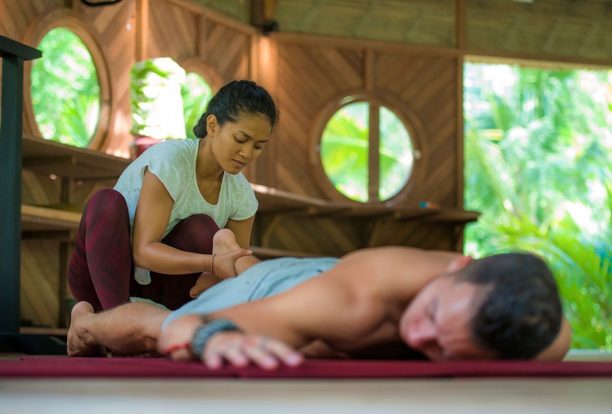 young beautiful and exotic Asian Indonesian therapist woman giving traditional Thai massage to man lying relaxed at tropical wellness spa in healthy natural lifestyle and body care